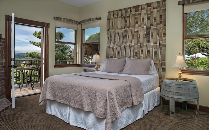 A bedroom with a queen bed, a barrel nightstand, and a balcony with table and chairs.