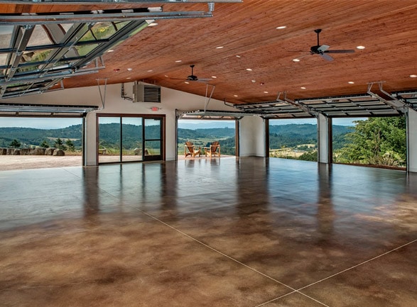An empty, modern hall with polished brown concrete floors, a wood ceiling, and wide open views of rolling hills.