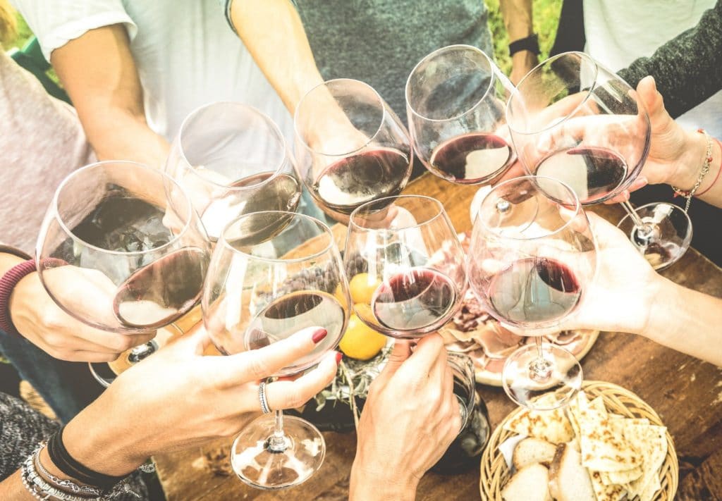 A group of people cheers with glasses of red wine held over a table with food.