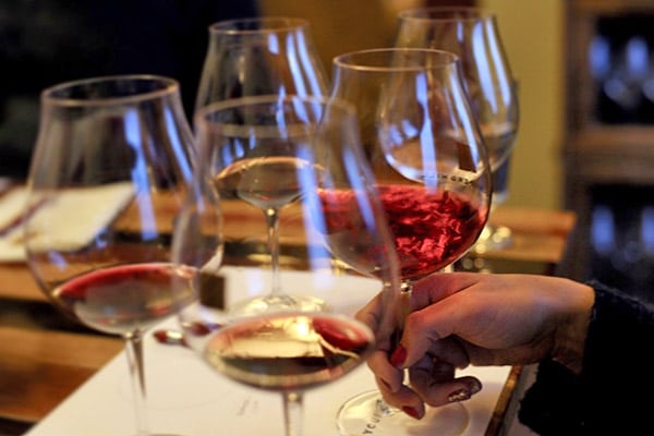 A hand holds a wine glass during a tasting, with several other wine glasses arranged on a table.